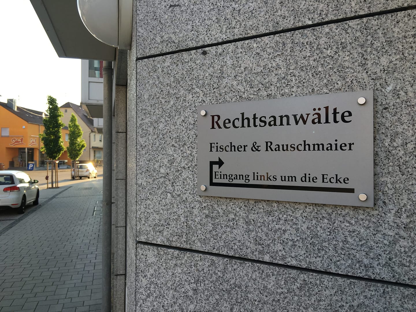 EIn Schild auf dem Rechtsanwälte Fischer & Rauschmaier steht, weist nach links um die Ecke zum EIngang.